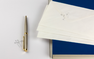 Gold pen on white desk with navy blue notebook and three envelopes