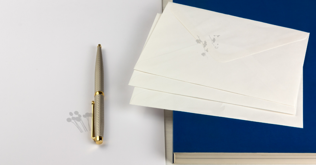 Gold pen on white desk with navy blue notebook and three envelopes